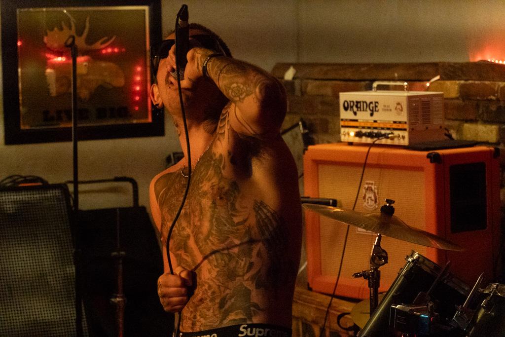 Tattooed vocalist on stage beside an orange amp