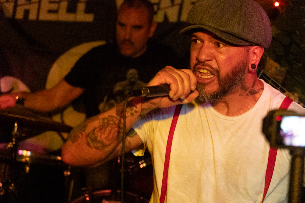 Vocalist in suspenders and flat cap shouting into the mic