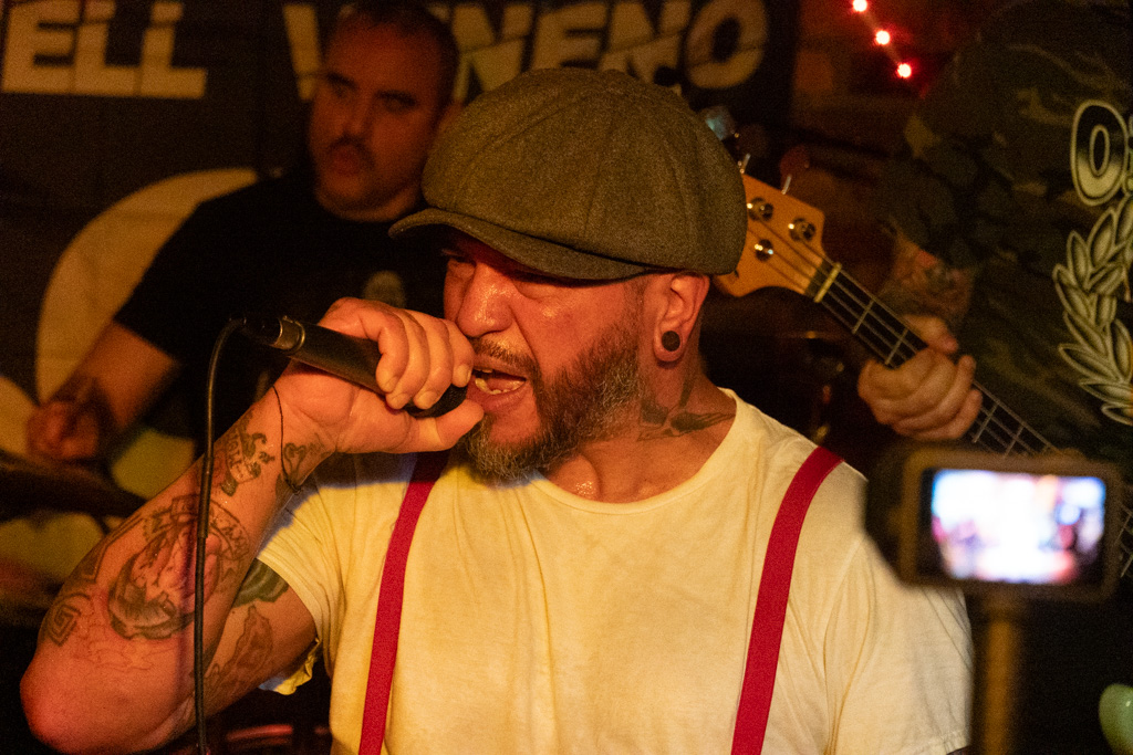 Vocalist in suspenders mid-verse with a phone filming nearby