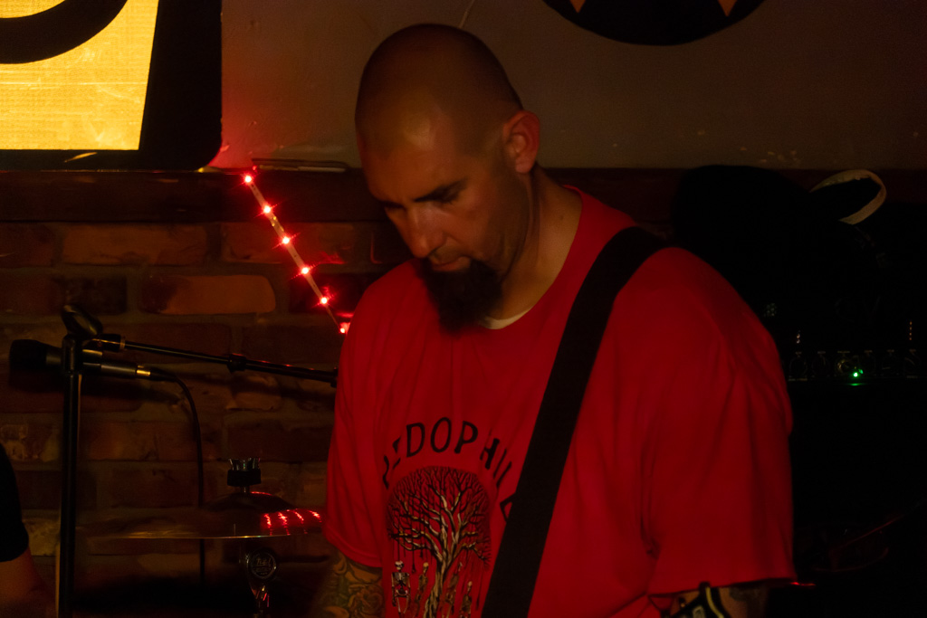 Guitarist in a red shirt looking down at his guitar